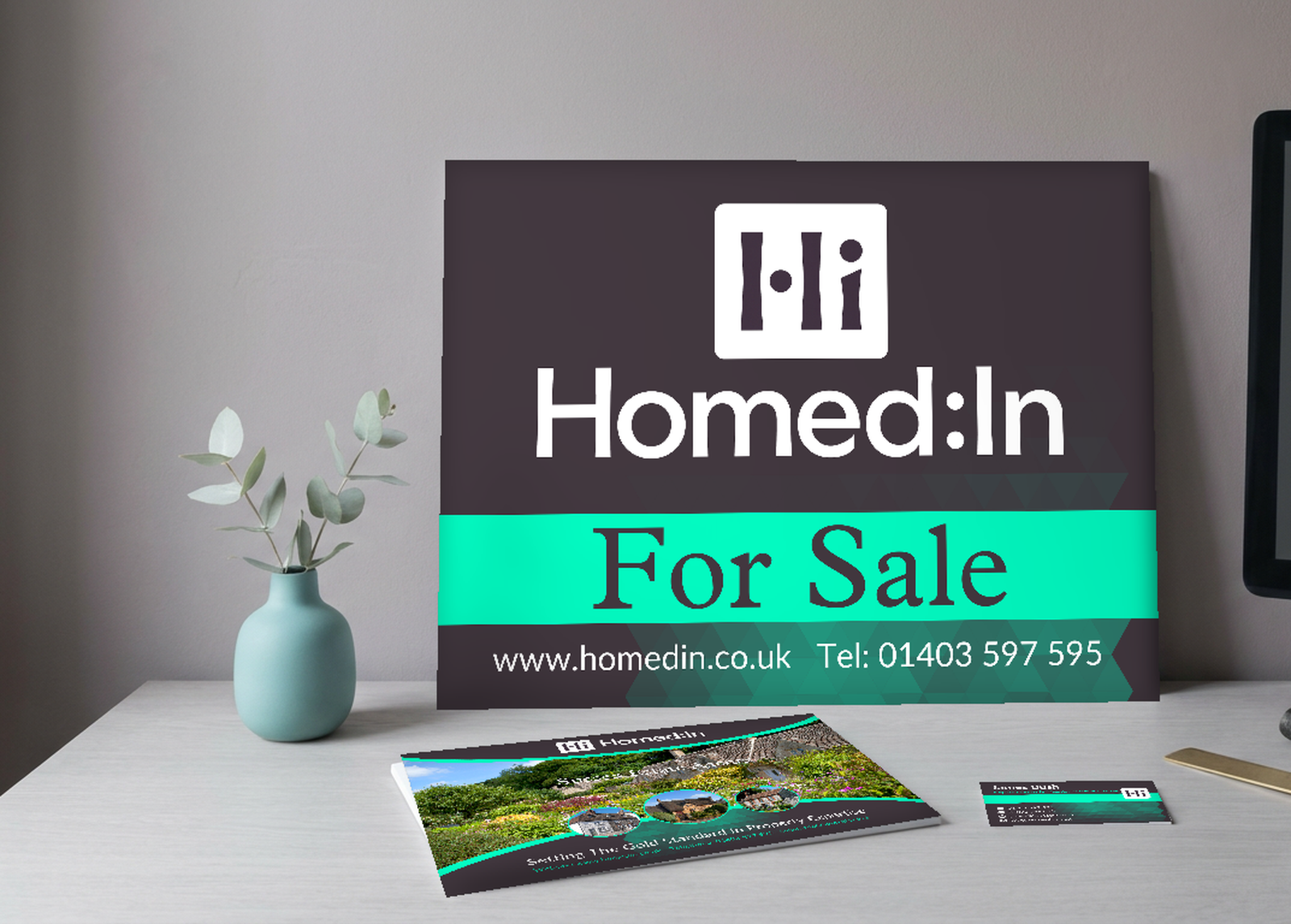 A Homed:In For Sale board designed by PWDP, standing on a studio desk beside a monitor